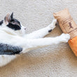 Load image into Gallery viewer, P.L.A.Y. Feline Frenzy Kicker - Tuna Baguette Toy being reached out to by a black and white cat on the carpet