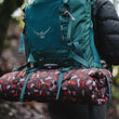 Load image into Gallery viewer, Scout & About Outdoor Chill Pad in Mocha strapped onto a hiking backpack being worn by a hiker