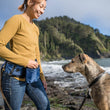 Load image into Gallery viewer, P.L.A.Y.&#39;s Explorer Pack in Waterfall Blue on a dog mom giving her dog a treat out of the treat pouch on beach with dog staring intently

