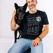 Load image into Gallery viewer, P.L.A.Y. Dog Dad Humanitee - T-Shirt modeled on dog dad sitting on his knees with his beautiful black dog over his shoulder both looking at the camera smiling
