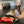 Load image into Gallery viewer, Clive &amp; Bacon x P.L.A.Y. Crispy Bacon Toy - in pan on stove with black and white dog wearing a chef&#39;s coat and hat behind it
