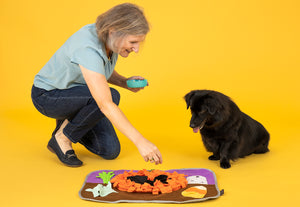 P.L.A.Y. Snuffle Mat - Halloween-themed with mom sprinkling treats onto mat with dog watching