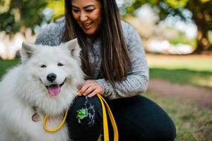 Proper Pup Poop Bag Dispensers from P.L.A.Y. - Kalahari Black on yellow leash being held by human as she smiles at her fluffy white dog also smiling