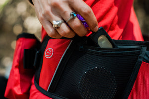 P.L.A.Y.'s Explorer Pack in Lava Red with hand pulling keys out of zippered pocket